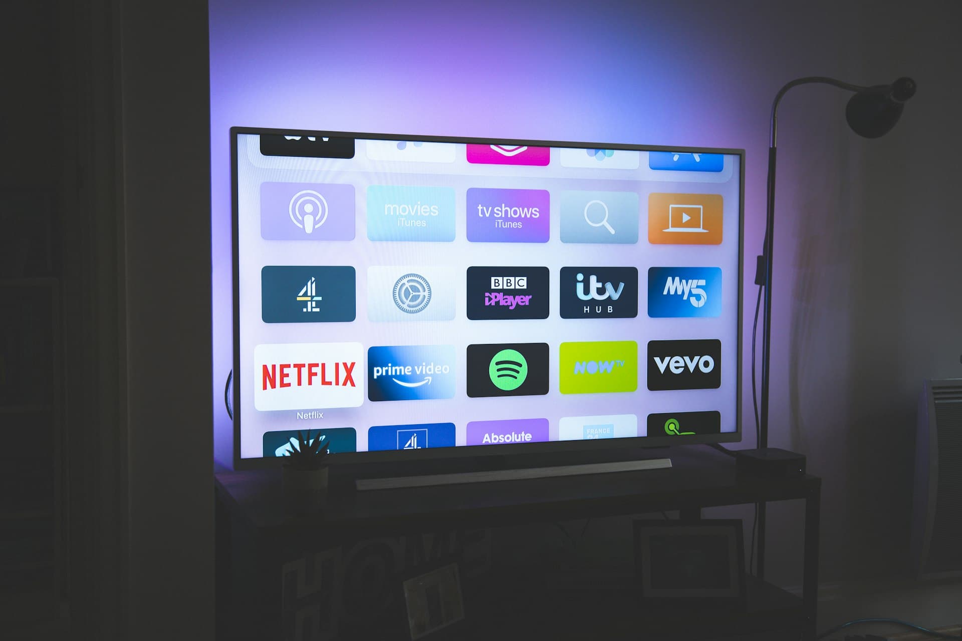 A dark living room lit only by the purple ambient glow of a flat-screen TV showing a grid of streaming app tiles.