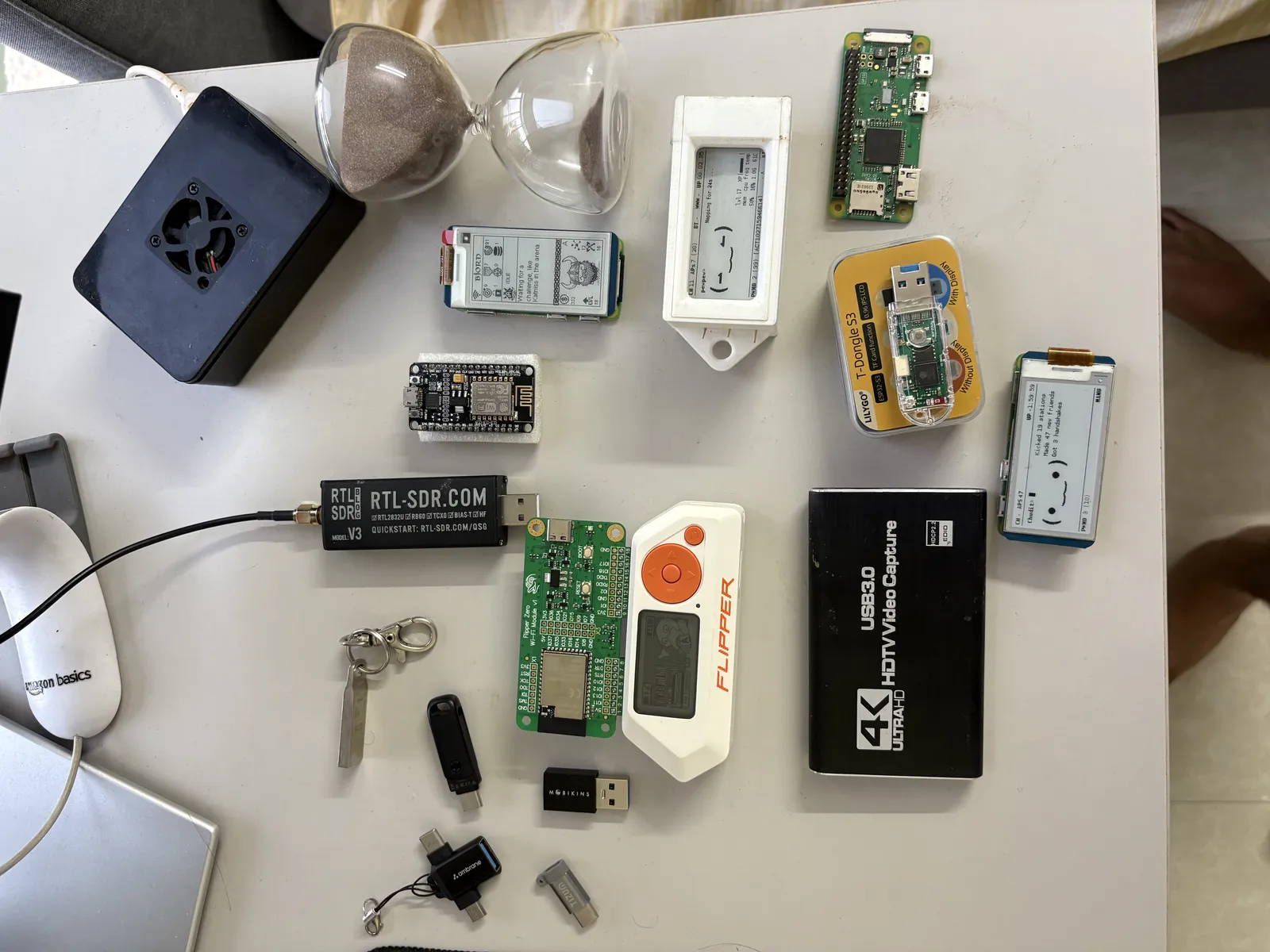 The workbench: SDR, Flipper Zero, Pwnagotchi, a Pi Zero, and an hourglass.